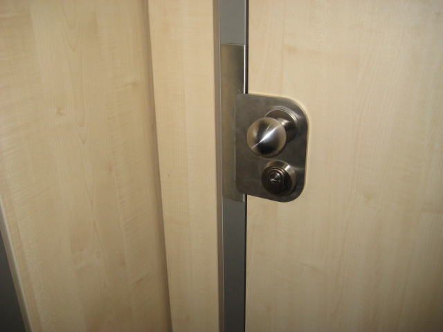 Nach außen öffnende Tür mit den Türspalt überdeckendem Sonderbeschlag und Rahmenverstärkung.